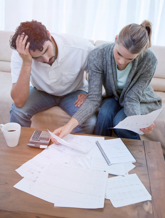 A couple sits on the floor, looking stressed while reviewing financial documents and contacting a Montgomery County Criminal Defense Lawyer. Papers and blueprints are spread around them.