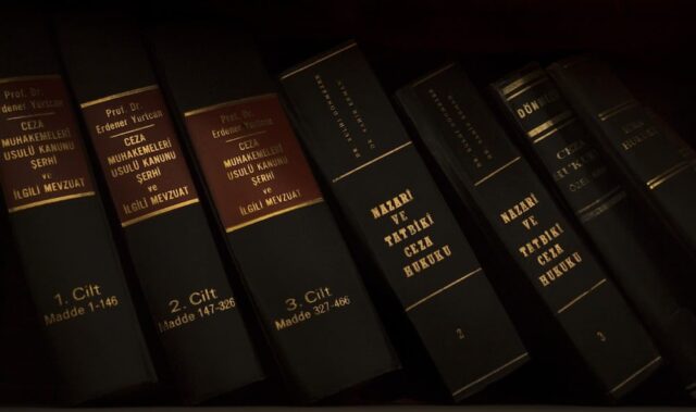 A row of old books on a shelf with gold lettering on the spines, highlighting various titles and volume numbers, including legal volumes related to assault in Pennsylvania, illuminated dimly.
