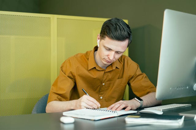 man writing notes and using computer